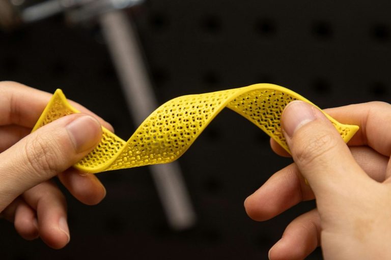 Hände halten ein gewundenes, gelbes Stück TPU mit feinen Löchern.
